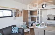 Intérieur de lodge moderne avec mezzanine, cuisine, coin repas, canapé et une décoration lumineuse et cosy.