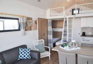 Acogedora cabaña moderna con altillo, cocina, mesa de comedor y sala decorada en tonos claros y frescos.