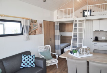 Modern lodge interior featuring a loft bed, kitchenette, dining area, couch, and bright contemporary decor.