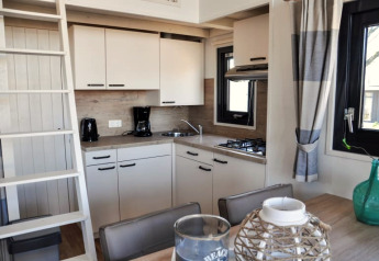 Cuisine moderne de lodge avec armoires blanches, cafetière, gazinière, fenêtres et table à manger décorée.