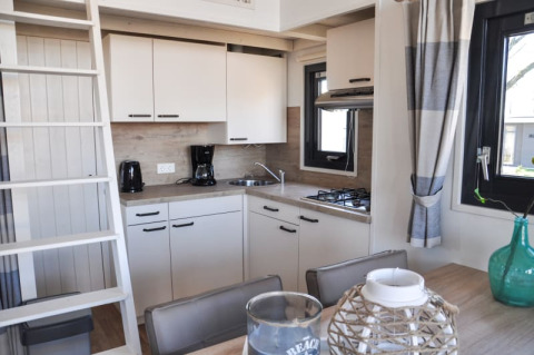 Cocina moderna en una cabaña con armarios blancos, cafetera, estufa de gas y mesa de comedor con decoración.