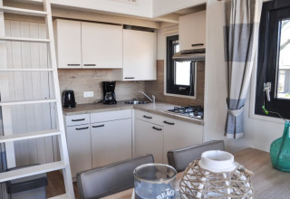 Cocina moderna en una cabaña con armarios blancos, cafetera, estufa de gas y mesa de comedor con decoración.