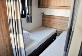 Zimmer in einer Lodge mit zwei Einzelbetten, Holzwänden und grauen Vorhängen, modernes Ambiente.