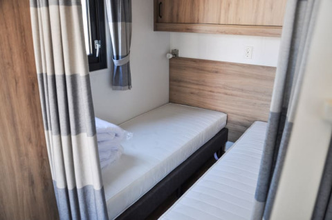 Habitación de lodge con dos camas individuales, paneles de madera, ventana y cortinas grises modernas.