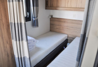 Lodge room with two single beds, wooden paneling, window, and gray curtains in a bright modern style.