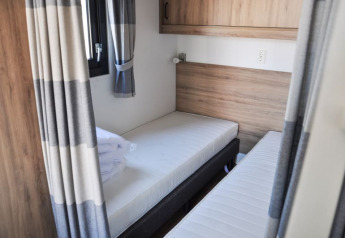 Værelse på en lodge med to enkeltsenge, træpaneler, grågardiner og vindue, lyst og moderne design.