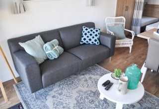 Sala de lodge moderna con sofá gris, cojines, mesa blanca, plantas, tazas y decoración elegante.
