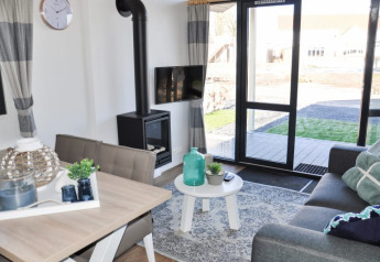 Lyst og moderne opholdsstue i en lodge med sofagruppe, spisebord, pejs, TV og udsigt over haven.