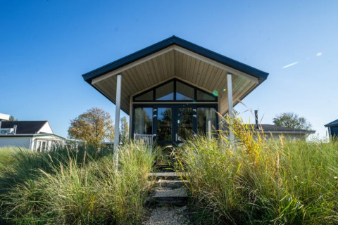 Photo of a modern lodge with large windows, surrounded by tall grasses and a clear blue sky above.