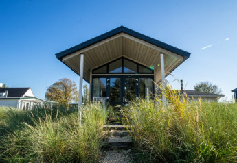Photo of a modern lodge with large windows, surrounded by tall grasses and a clear blue sky above.