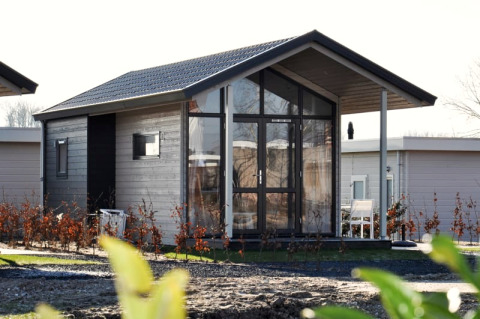 Modernes Holzhaus mit Glasfront und Veranda, umgeben von Sträuchern und weiteren Lodges im Hintergrund.