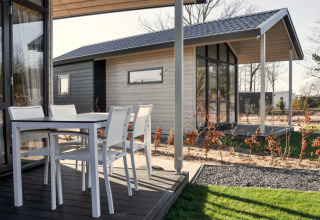 Terrasse eines modernen Lodges mit weißen Gartenmöbeln und Blick auf ein weiteres Lodge im Hintergrund.