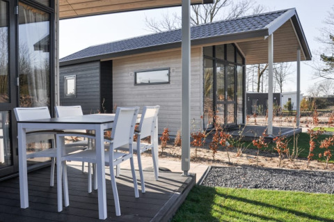 Terrasse eines modernen Lodges mit weißen Gartenmöbeln und Blick auf ein weiteres Lodge im Hintergrund.