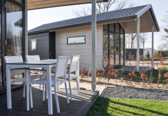 Udendørs terrasse ved en moderne lodge med hvide havemøbler og udsigt til en anden lodge i baggrunden.