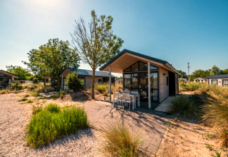 Moderne Ferienlodge mit Terrasse und Sitzbereich, umgeben von Natur und klarem blauen Himmel.