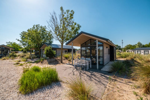 Modern lodge with patio and outdoor furniture, surrounded by greenery under a clear blue sky.