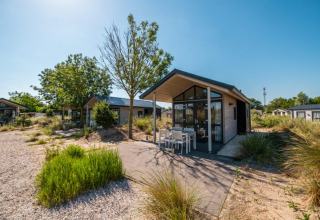 Lodge moderno con terraza y muebles de exterior, rodeado de vegetación y cielo azul despejado.