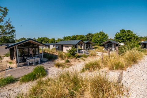 Cabañas modernas rodeadas de caminos arenosos y vegetación bajo un cielo azul, ideales para descansar.
