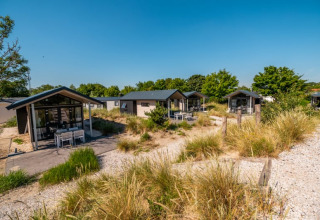 Cabañas modernas rodeadas de caminos arenosos y vegetación bajo un cielo azul, ideales para descansar.