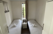 Habitación pequeña de lodge con dos camas individuales, ropa de cama blanca, mesita y ventana con vista.