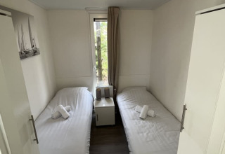 Petite chambre d’un lodge avec deux lits simples, linge blanc, table de chevet et fenêtre donnant sur l’extérieur.