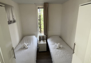 Habitación pequeña de lodge con dos camas individuales, ropa de cama blanca, mesita y ventana con vista.