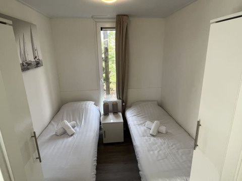 Habitación pequeña de lodge con dos camas individuales, ropa de cama blanca, mesita y ventana con vista.