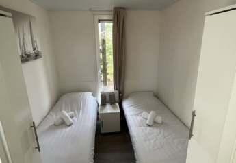 Petite chambre d’un lodge avec deux lits simples, linge blanc, table de chevet et fenêtre donnant sur l’extérieur.