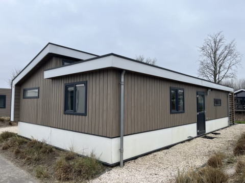 Un pavillon en bois moderne avec des cadres de fenêtres noirs, installé sur un chemin de gravier entouré d’herbe.