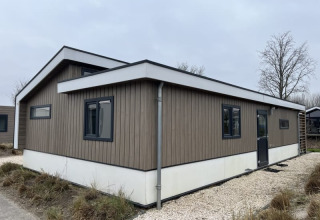 Una moderna cabaña de madera con marcos de ventana negros ubicada en un sendero de grava entre césped y árboles.