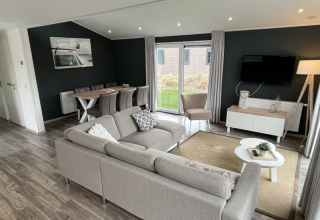 Modernes Lodge-Wohnzimmer mit grauem Ecksofa, Esstisch, großem Fenster, Teppich und Wand-TV.