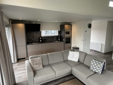 Interior de lodge moderno con cocina abierta, salón, sofá gris en esquina y una decoración elegante.