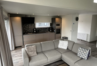 Interior de lodge moderno con cocina abierta, salón, sofá gris en esquina y una decoración elegante.