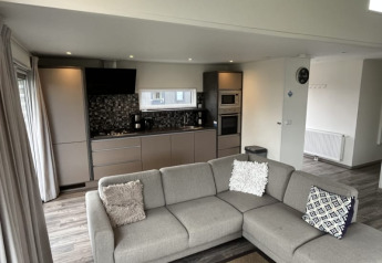 Interior de lodge moderno con cocina abierta, salón, sofá gris en esquina y una decoración elegante.