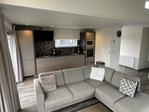 Interior moderno de lodge con cocina abierta, sofá en L, cojines decorativos y elegante decoración neutra.