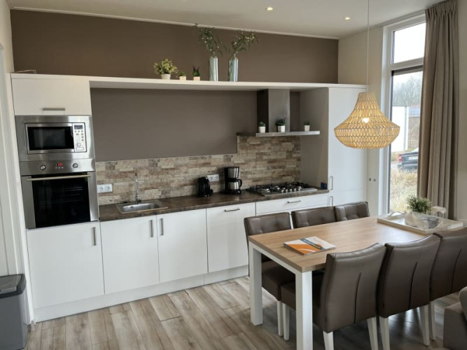 Cocina moderna en una cabaña, mesa de comedor, electrodomésticos y grandes ventanales soleados.