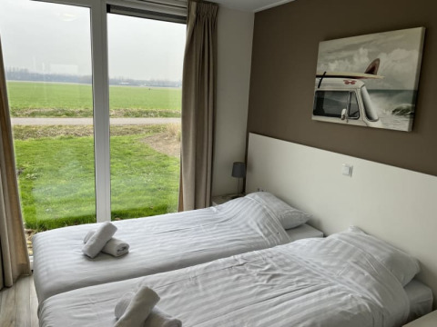 Chambre lumineuse d'un lodge avec deux lits simples, grandes fenêtres et vue sur un champ vert.