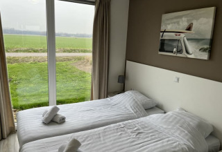 Helles Zimmer in einer Lodge mit zwei Einzelbetten, großen Fenstern und Blick auf eine grüne Wiese.