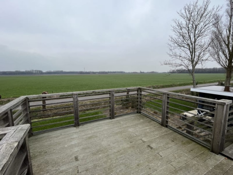 Vue depuis une terrasse en bois d’un lodge donnant sur des champs ouverts et des arbres sans feuilles sous ciel gris.