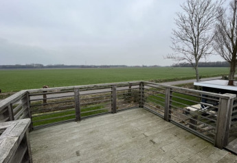 Vue depuis une terrasse en bois d’un lodge donnant sur des champs ouverts et des arbres sans feuilles sous ciel gris.