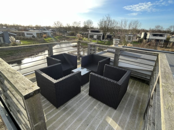 Terraza en la azotea de una cabaña con cuatro sillones de mimbre negros, mesa y vista a casas junto al canal.