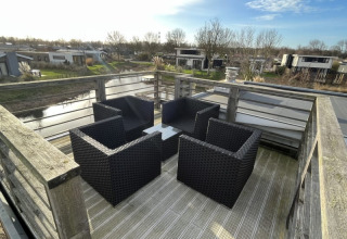 Terrasse sur le toit d’un lodge avec quatre fauteuils en osier noir, table et vue sur chalets et canal.