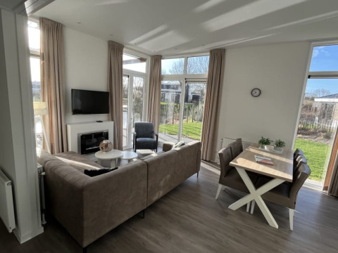 Helles, modernes Lodge-Wohnzimmer mit Sofa, Esstisch und großen Fenstern mit Blick auf den Garten.