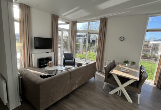 Helles, modernes Lodge-Wohnzimmer mit Sofa, Esstisch und großen Fenstern mit Blick auf den Garten.