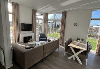 Salón moderno y luminoso de lodge con sofá, mesa de comedor y grandes ventanas con vistas al jardín.