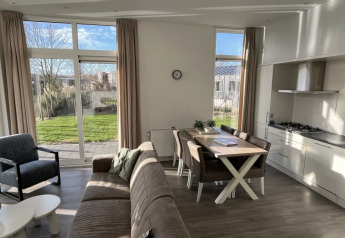 Bright, modern lodge living area with large windows, garden views, dining table, and open kitchen space.