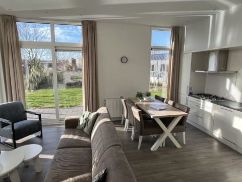 Sala de estar luminosa y moderna en una cabaña, con grandes ventanas, vistas al jardín y cocina abierta.