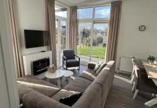 Salon moderne de lodge avec grandes fenêtres, canapé confortable et coin repas donnant sur le jardin.