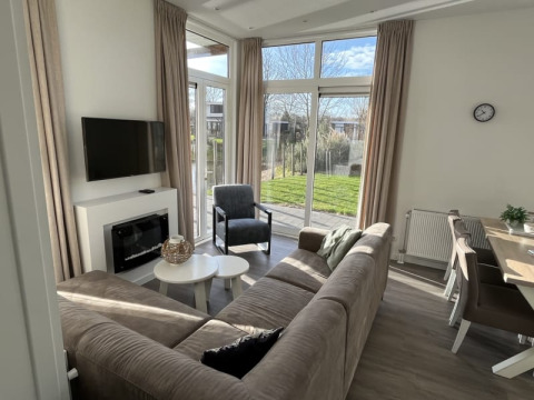 Moderne Lodge-Wohnzimmer mit großen Fenstern, gemütlichem Sofa und Essbereich mit Blick auf Garten.