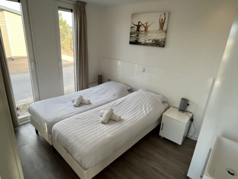 Chambre moderne en lodge avec deux lits simples, linge blanc, table de chevet et grande fenêtre vitrée.